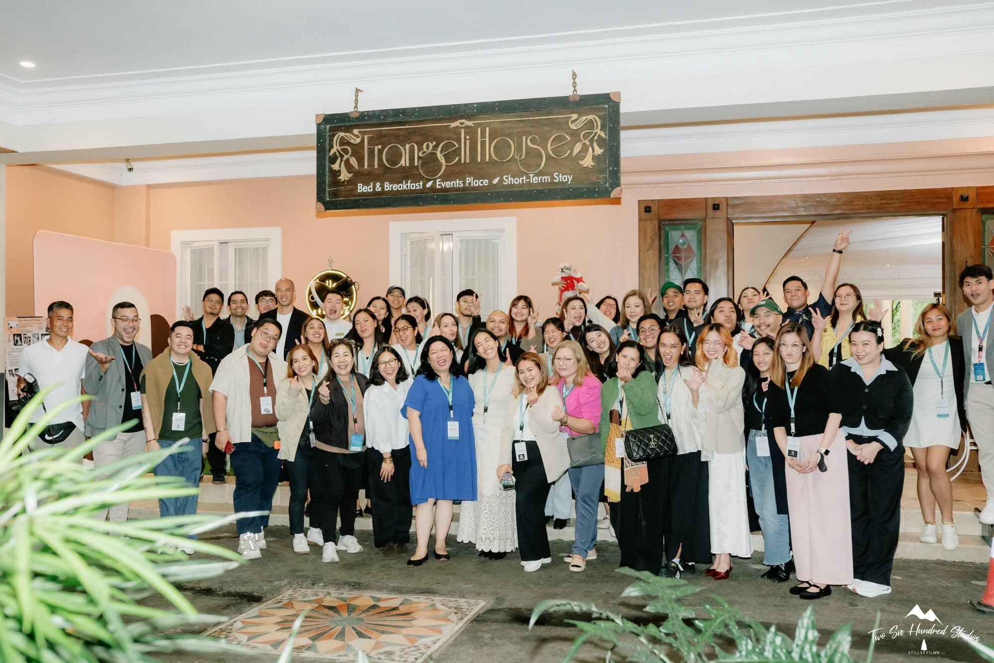 A large group of couples and wedding suppliers gathered for a photo beneath the Frangeli House sign