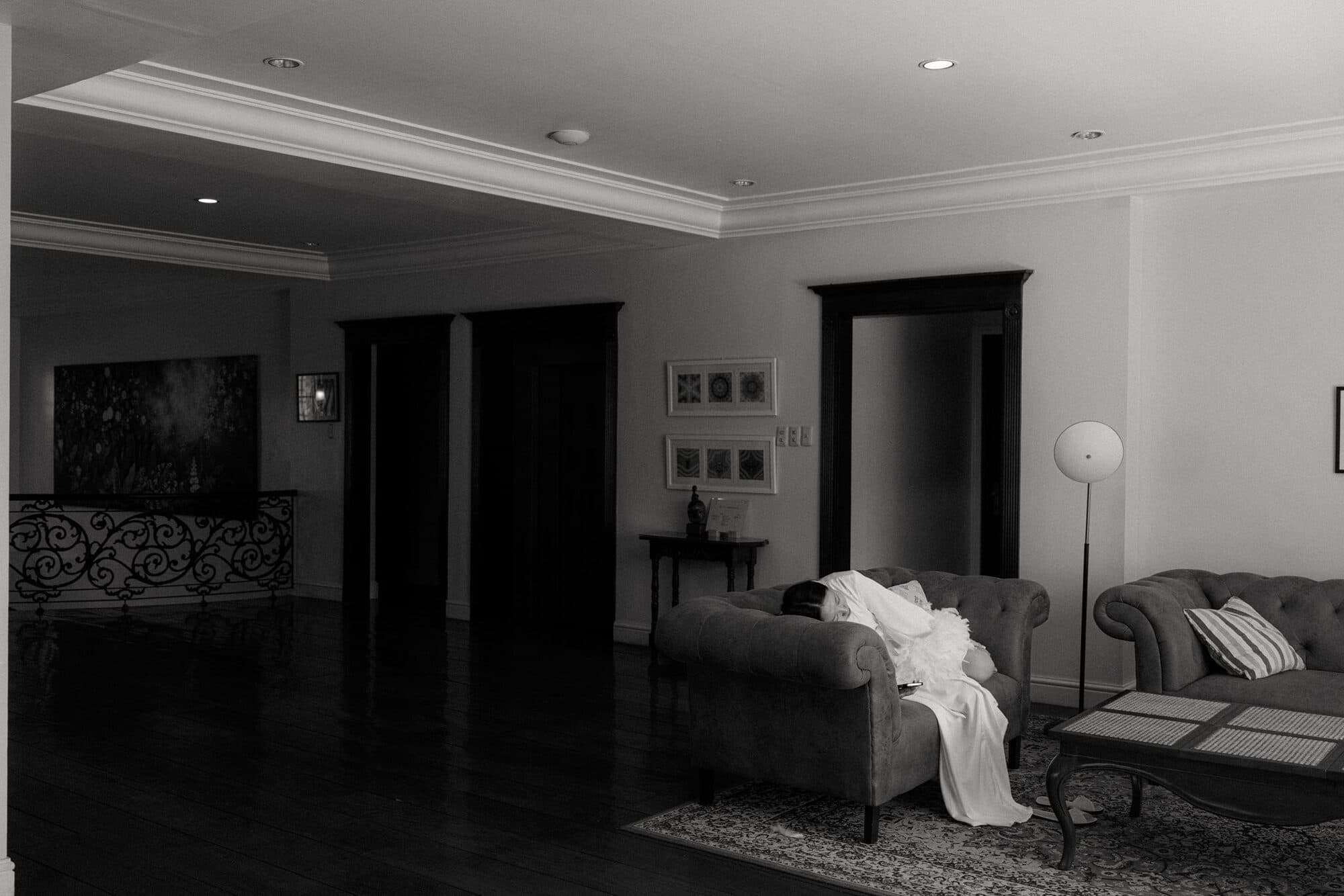 A bride's gown and veil laid across a velvet sofa in a quiet, dimly lit sitting room