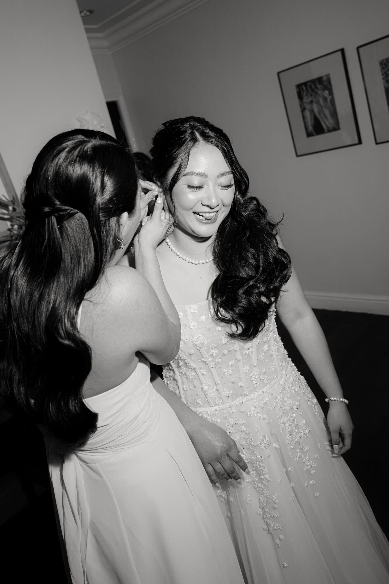 A bridesmaid fastening the bride’s earring as they get ready together in the morning