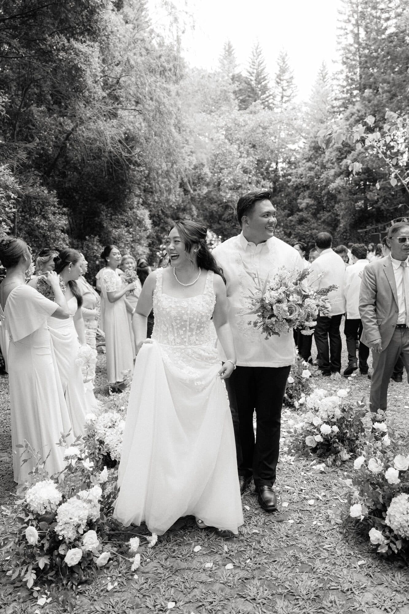 The newlyweds walking back down the aisle between guests and low white floral arrangements