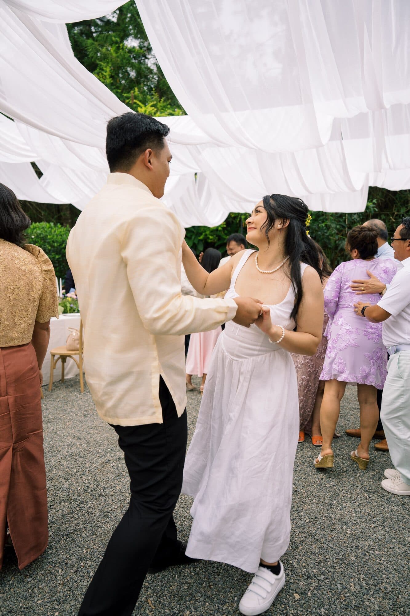 The couple dancing hand in hand among their guests beneath the white canopy