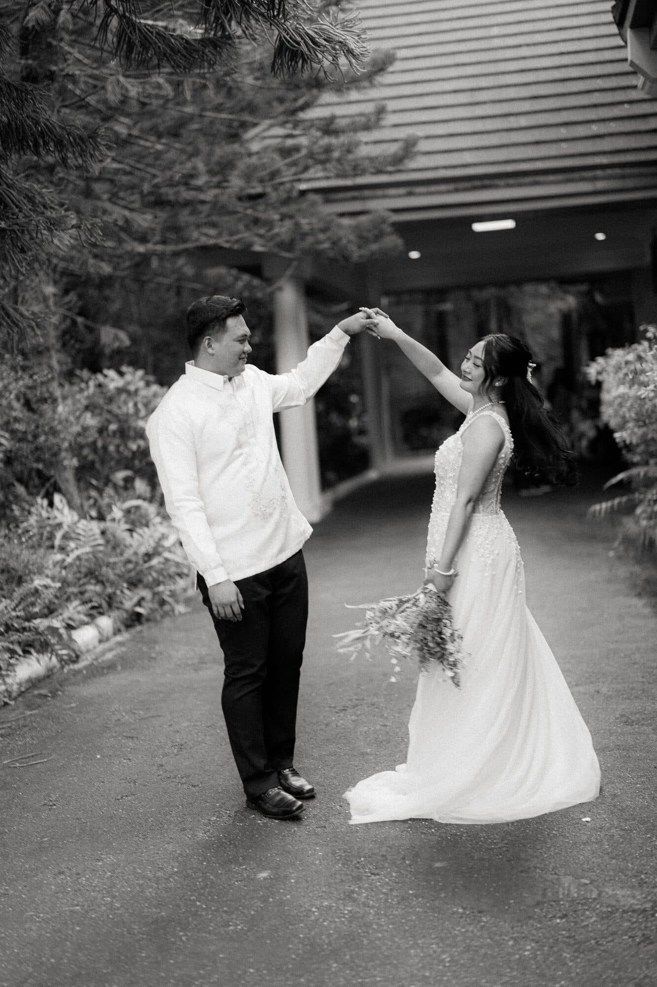 The groom twirling the bride on the driveway in front of the house, her train sweeping the ground