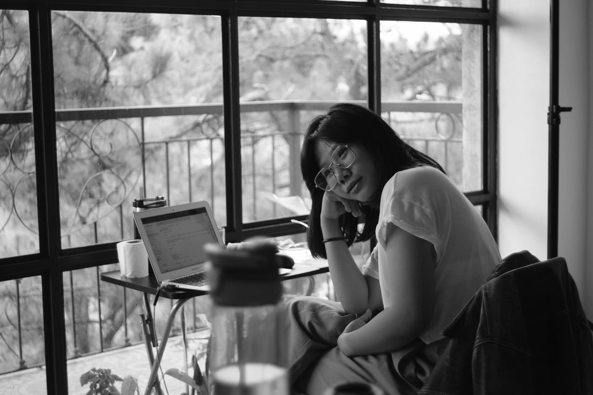 A wedding planner resting her chin on her hand at a window table beside her laptop, taking a quiet moment