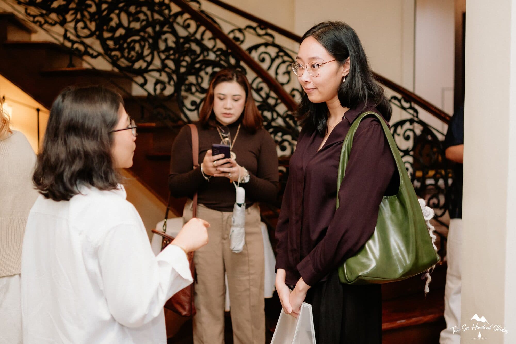 Three attendees talking beside the wrought-iron staircase of Frangeli House