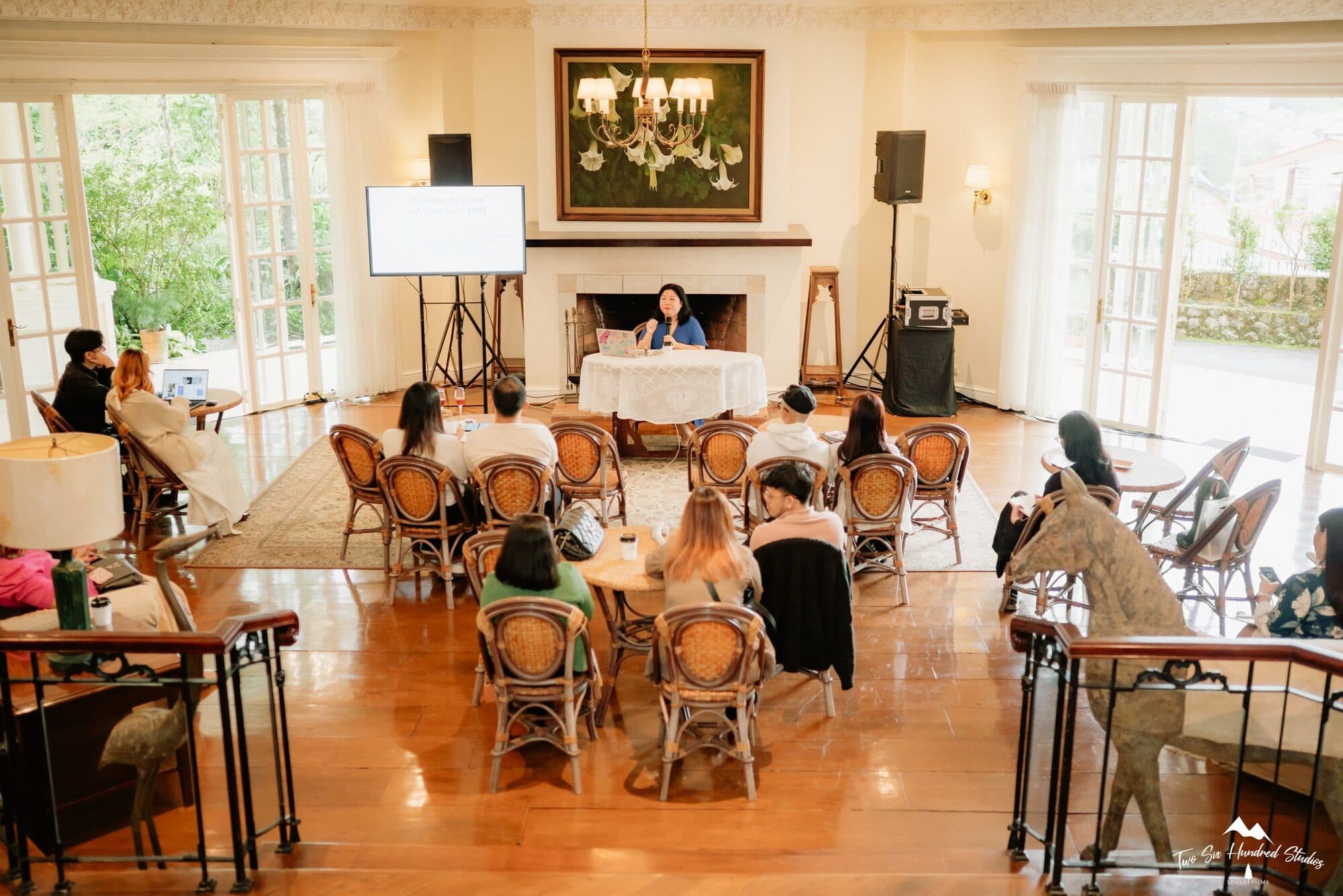 The sunroom set with rattan chairs facing a speaker seated by the fireplace during the morning talk
