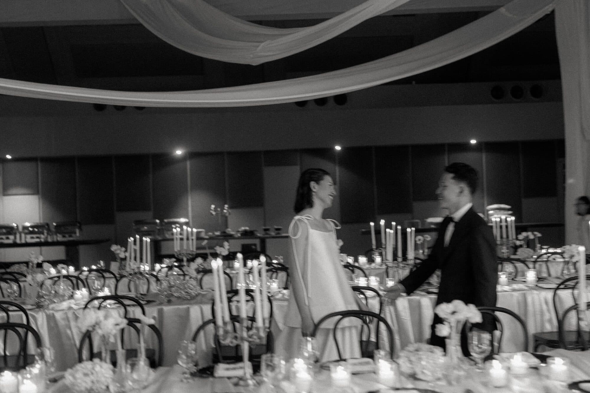 The bride and groom standing together at their reception table, smiling at each other among candles and glassware