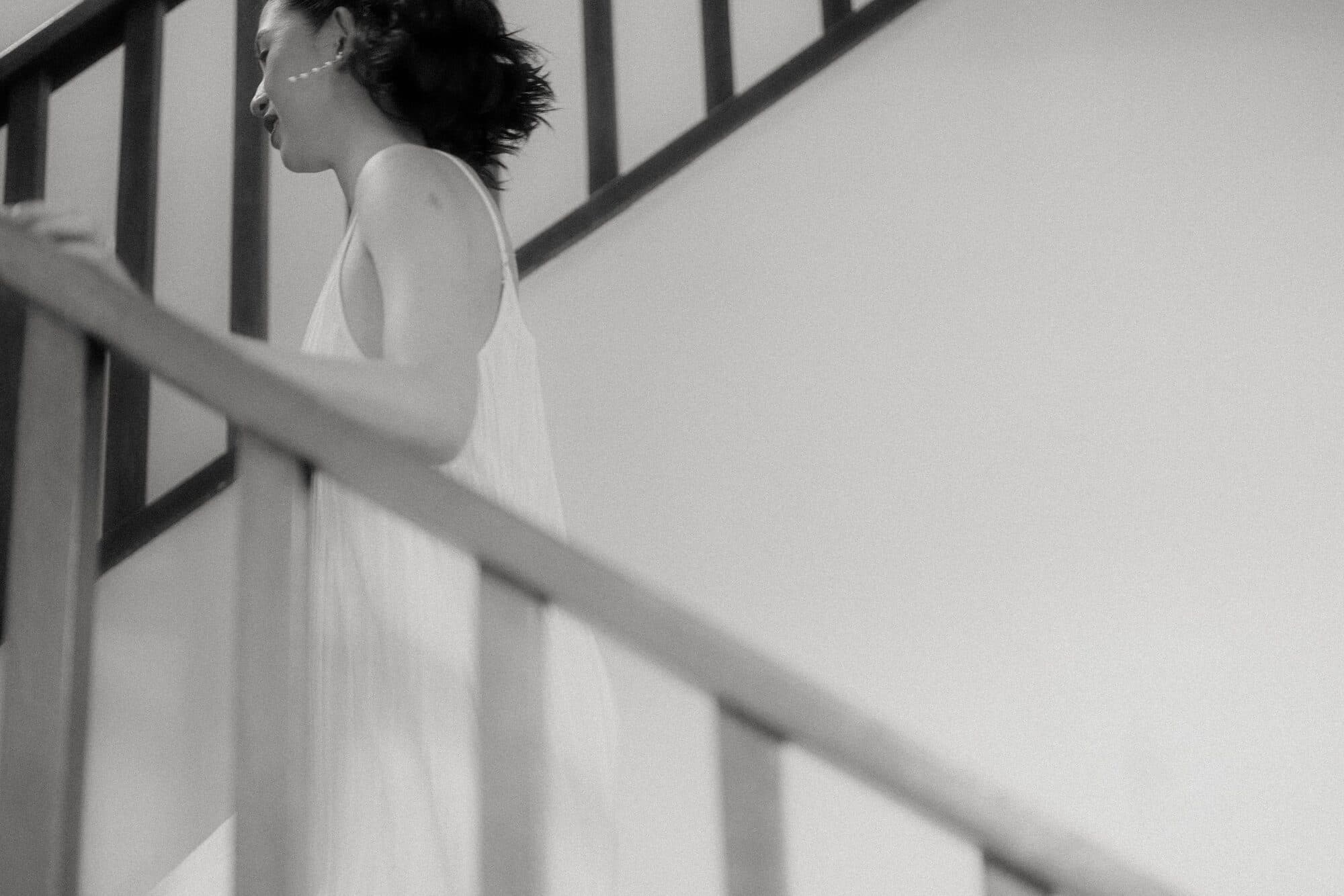The bride in a slip dress walking up a staircase on the morning of the wedding, smiling over her shoulder