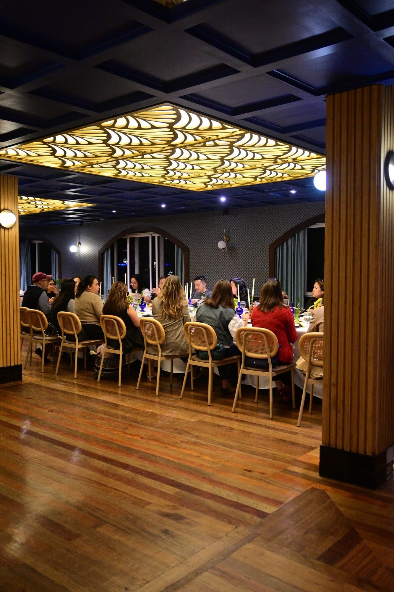 A wider view of the dining room, guests lining the long table above the polished wooden floor