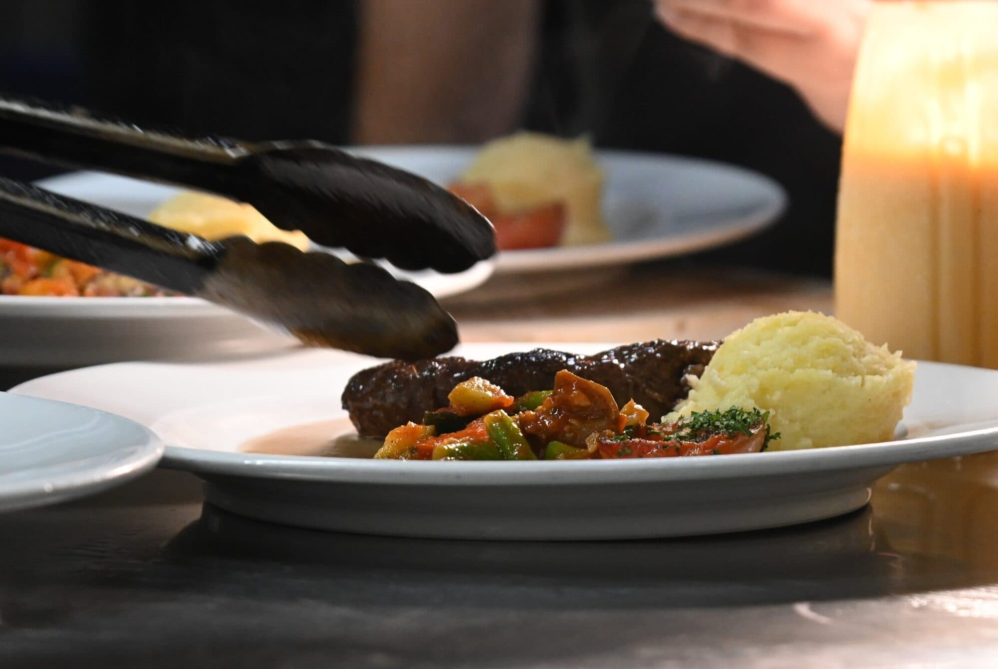 A grilled tenderloin steak with mashed potatoes and ratatouille being plated with tongs