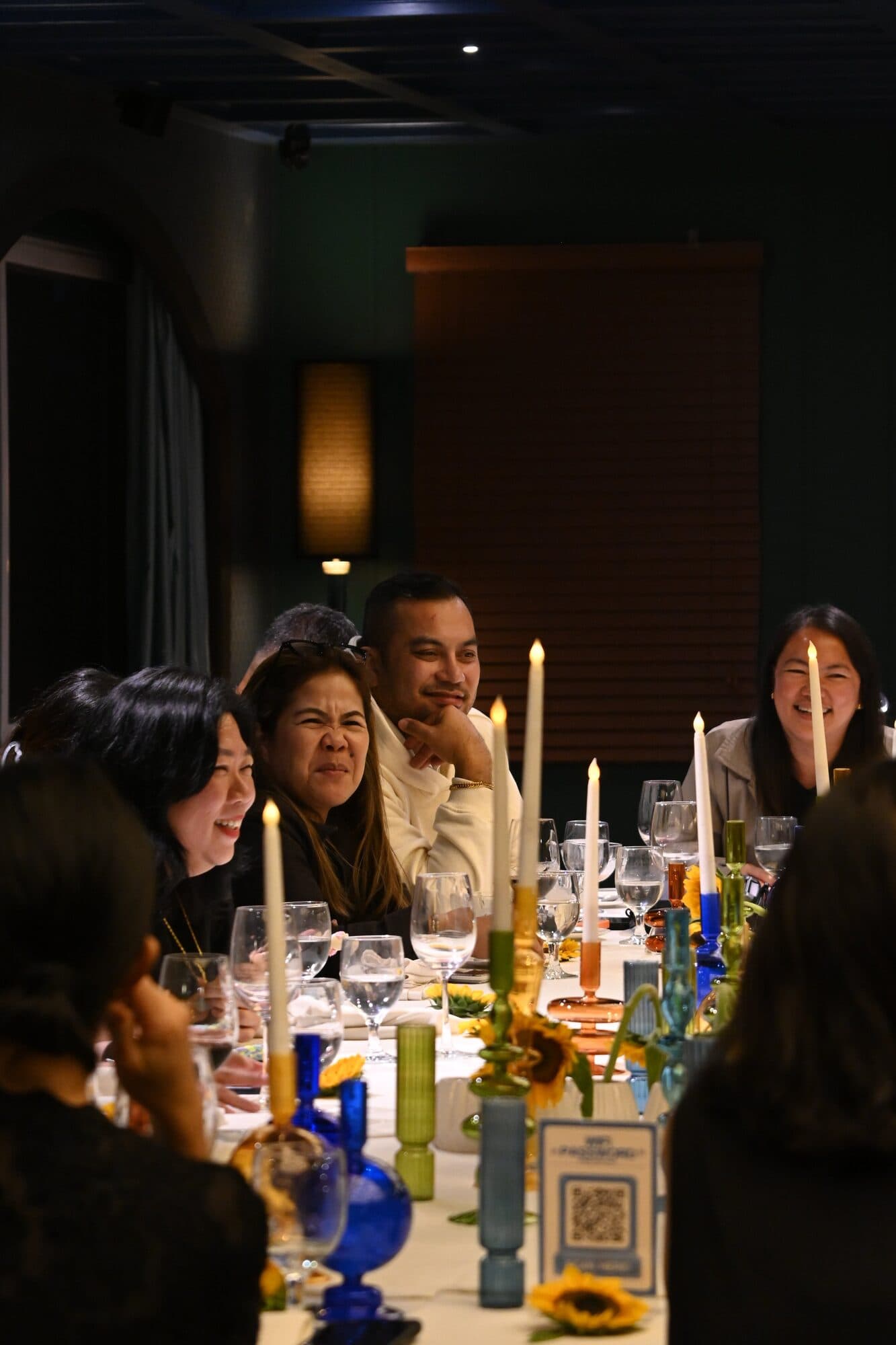 Guests smiling across the candlelit table, set with sunflowers and blue glassware